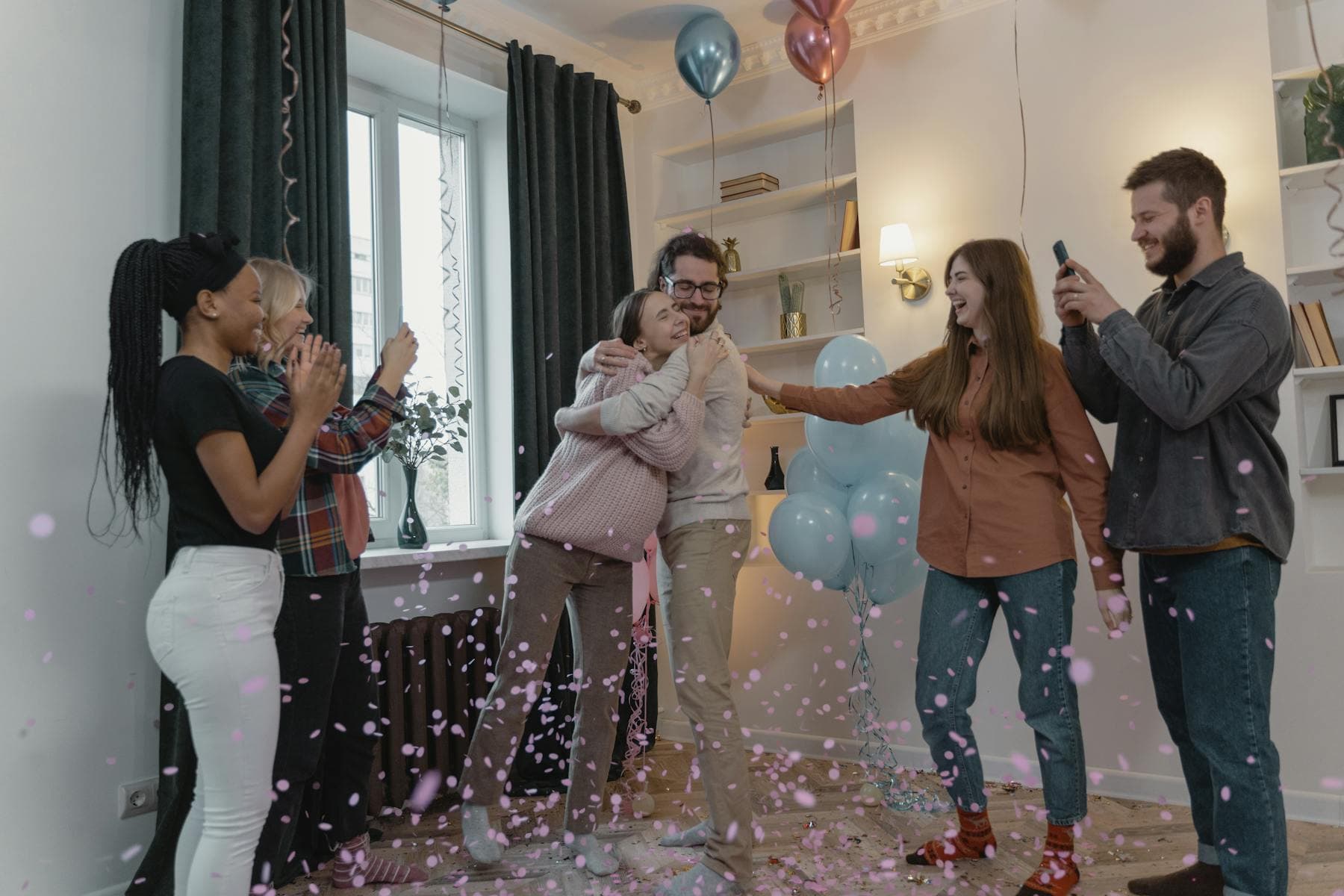 Friends celebrating a baby shower with balloons and confetti.